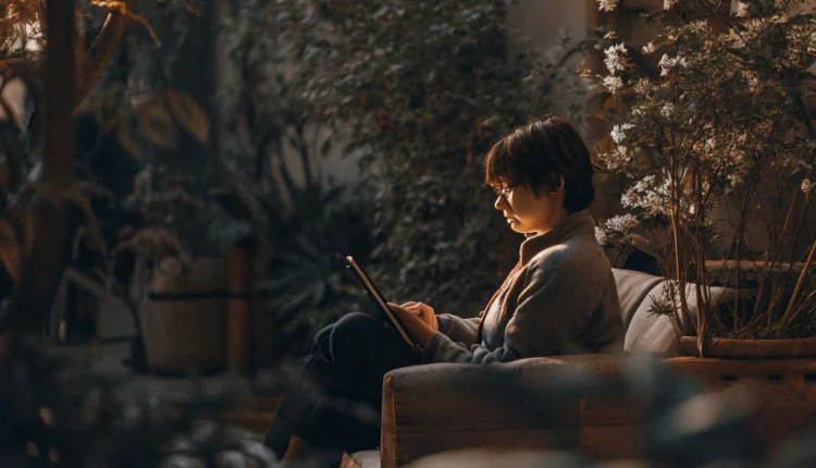 Young person in a sunlit garden, holding a tablet with a calm expression